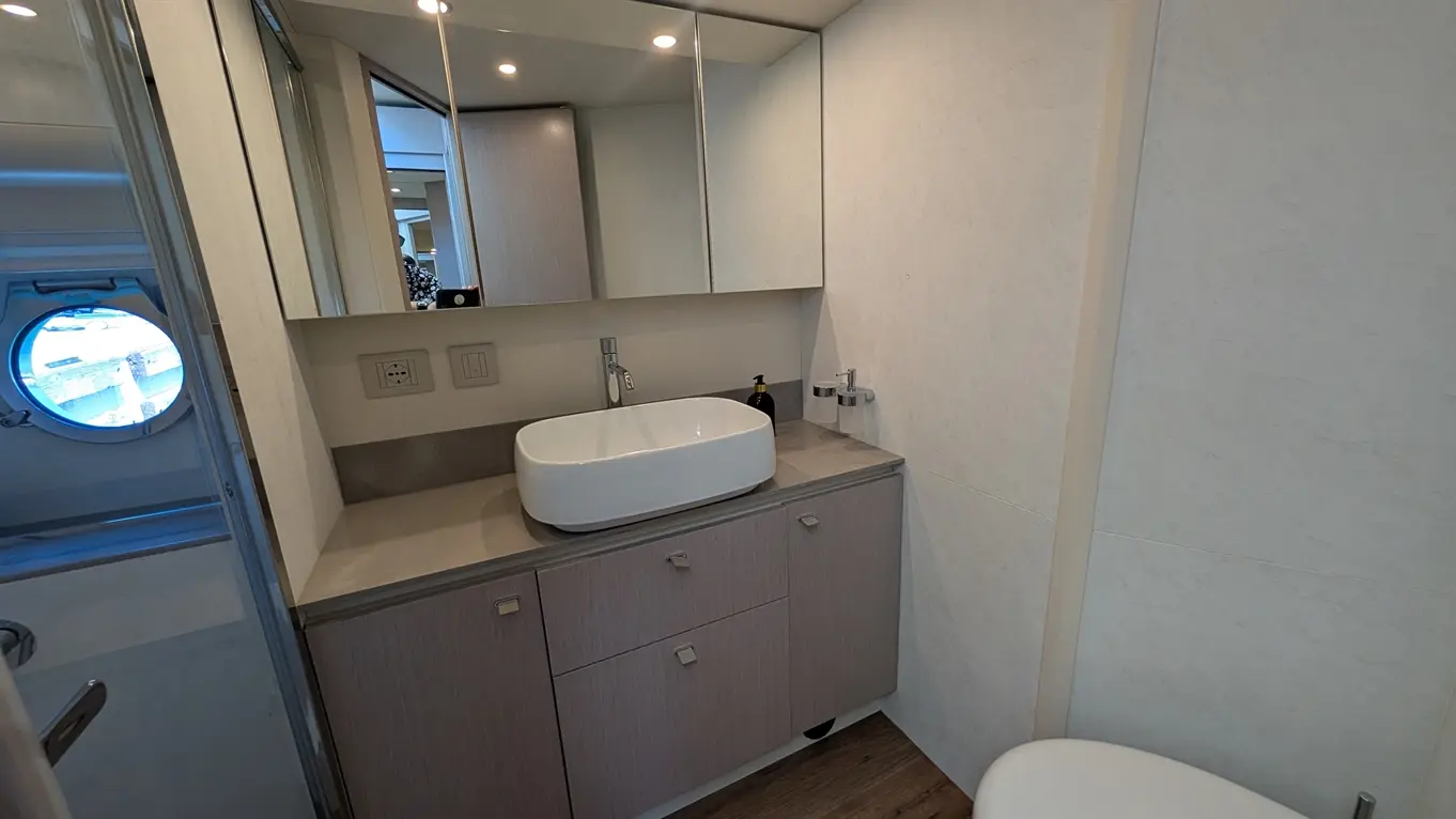 Modern bathroom featuring a large, white basin on a grey countertop, wooden cabinetry, mirrors, and a porthole window.